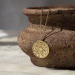 gold moonphase round pendant necklace hanging on a ceramic dish with shadows on a fabric surface