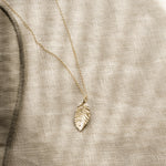 gold leaf shaped pendant necklace on a textured beige fabric with striped shadows