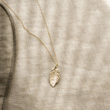 gold leaf shaped pendant necklace on a textured beige fabric with striped shadows
