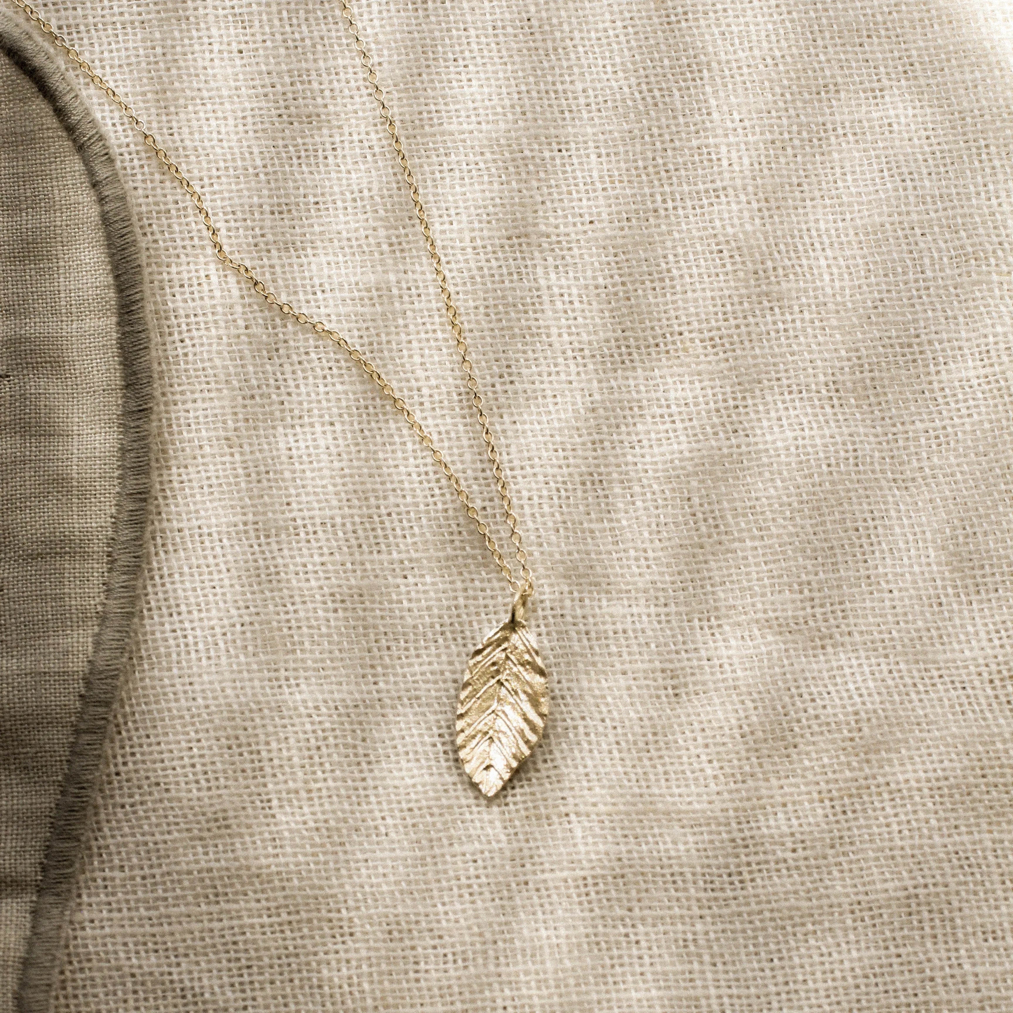 gold leaf shaped pendant necklace on a textured beige fabric with striped shadows