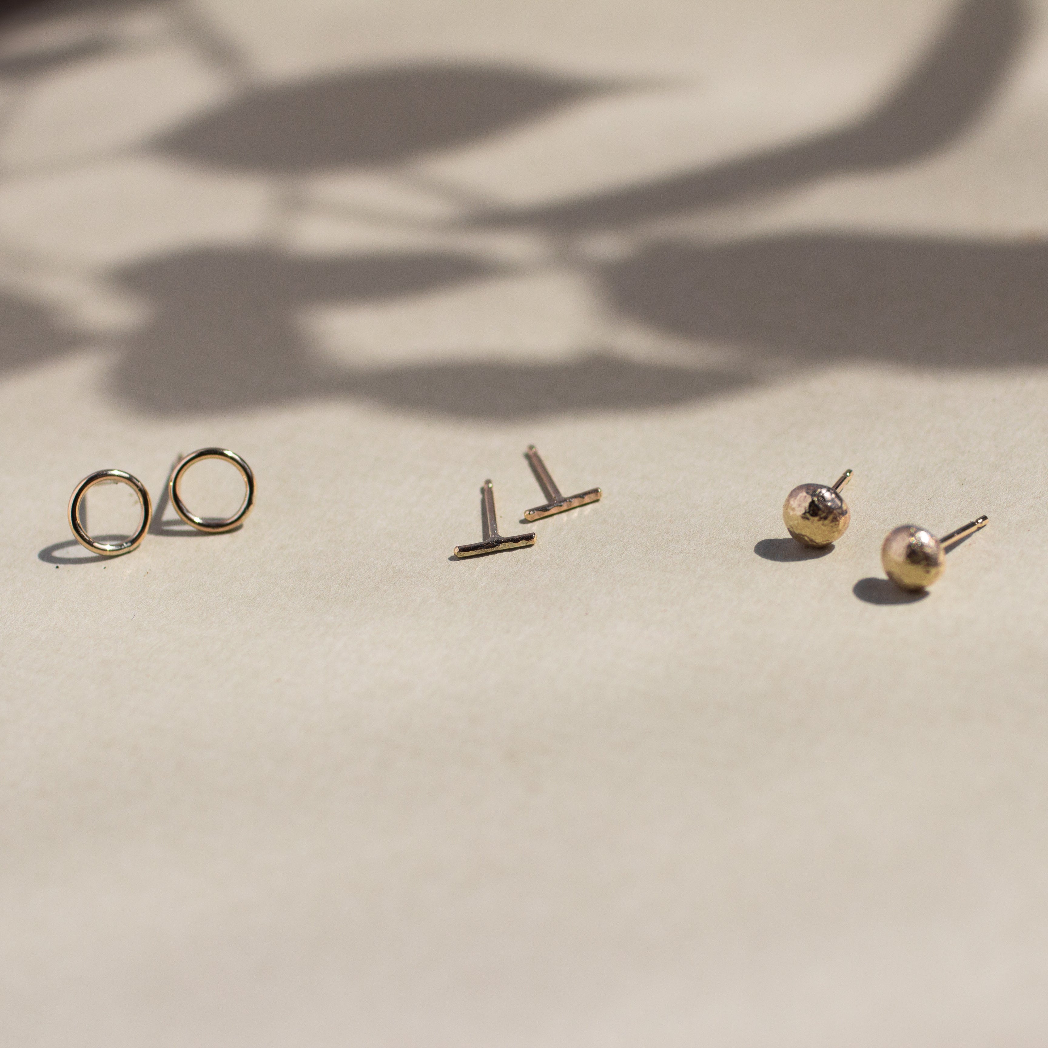 circle, bar and pebble gold stud earrings with leaf shadow