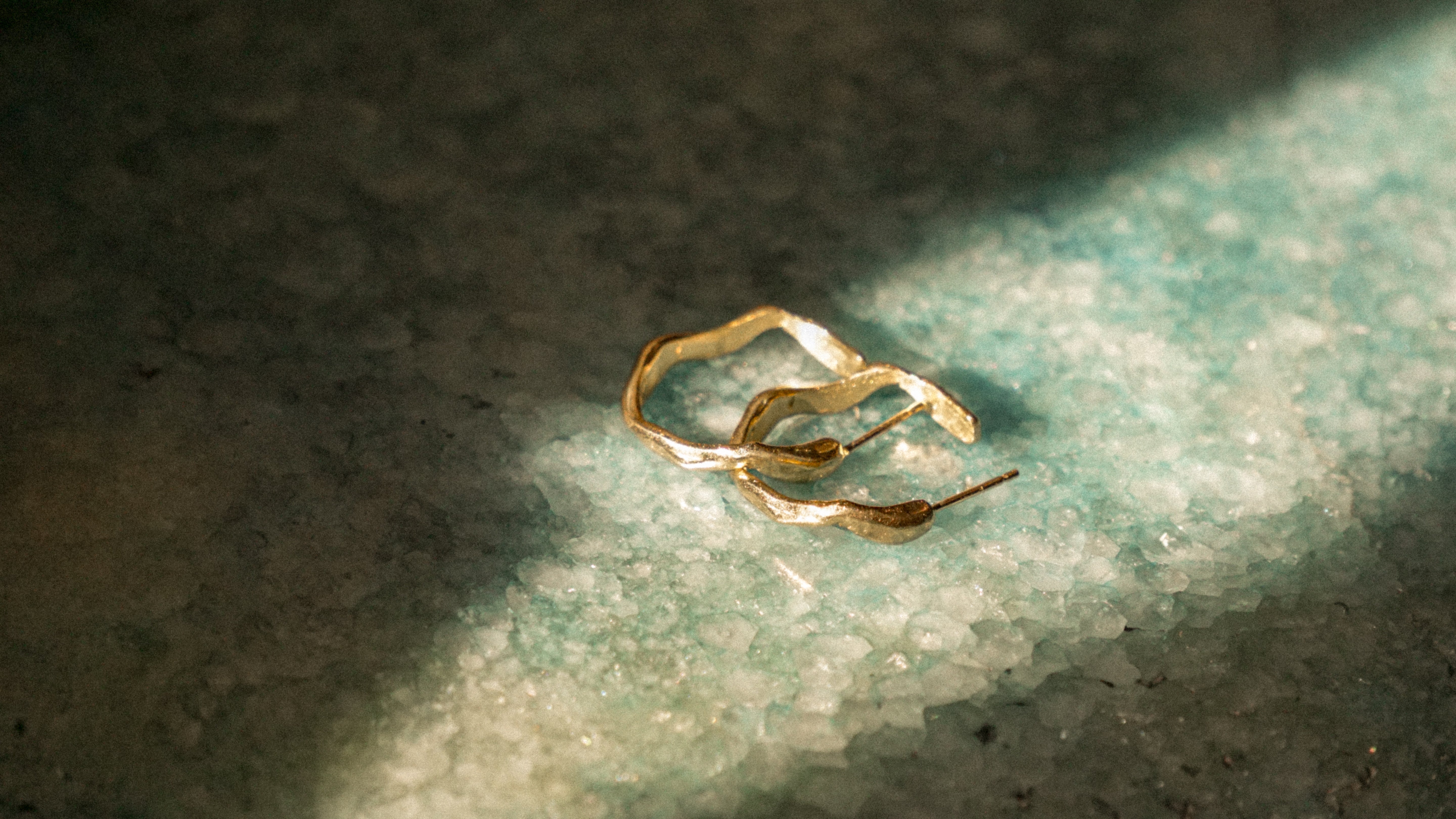 solid gold wave hoop earrings on green crystal surface