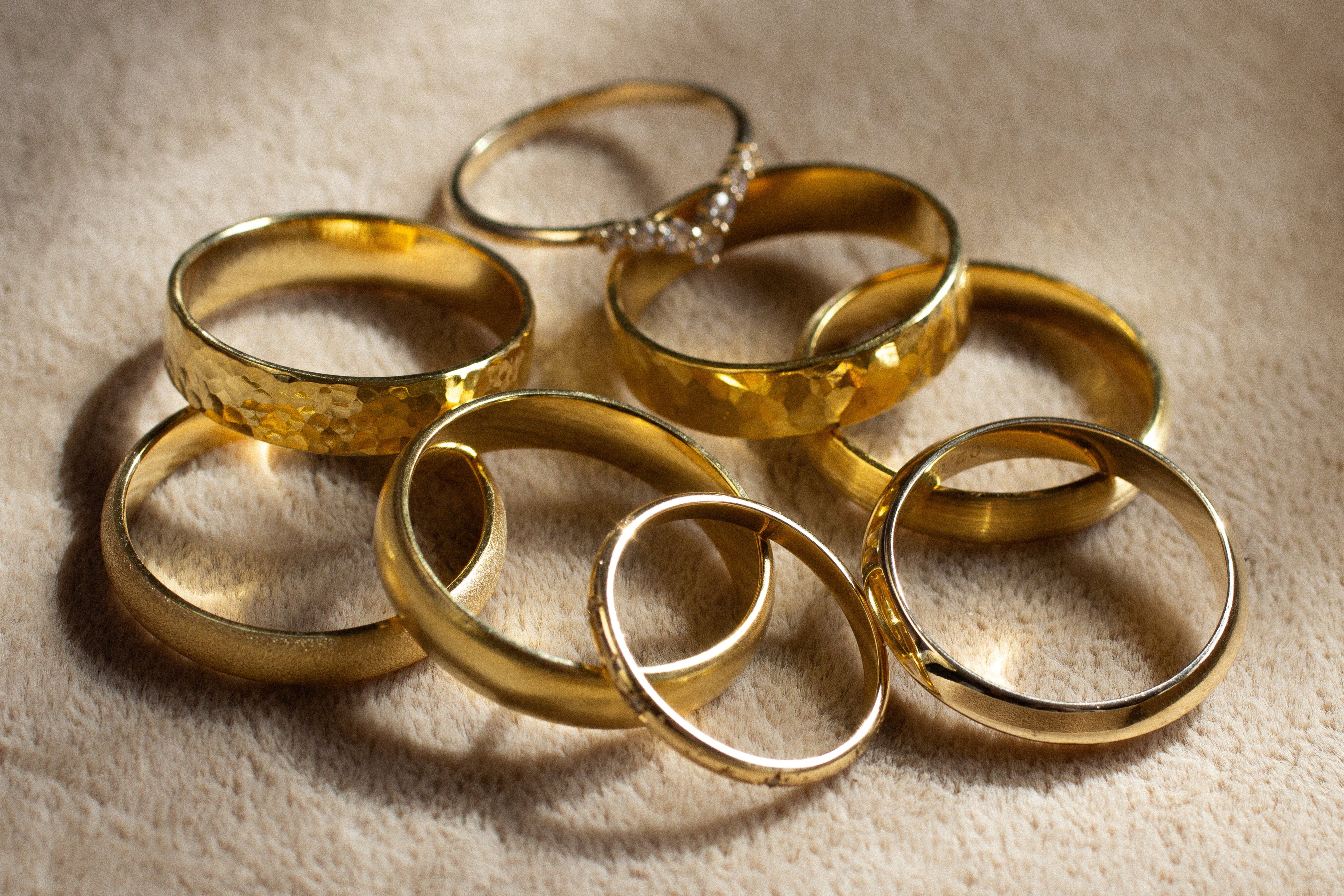 eight gold wedding rings in pile with different textures with shadows