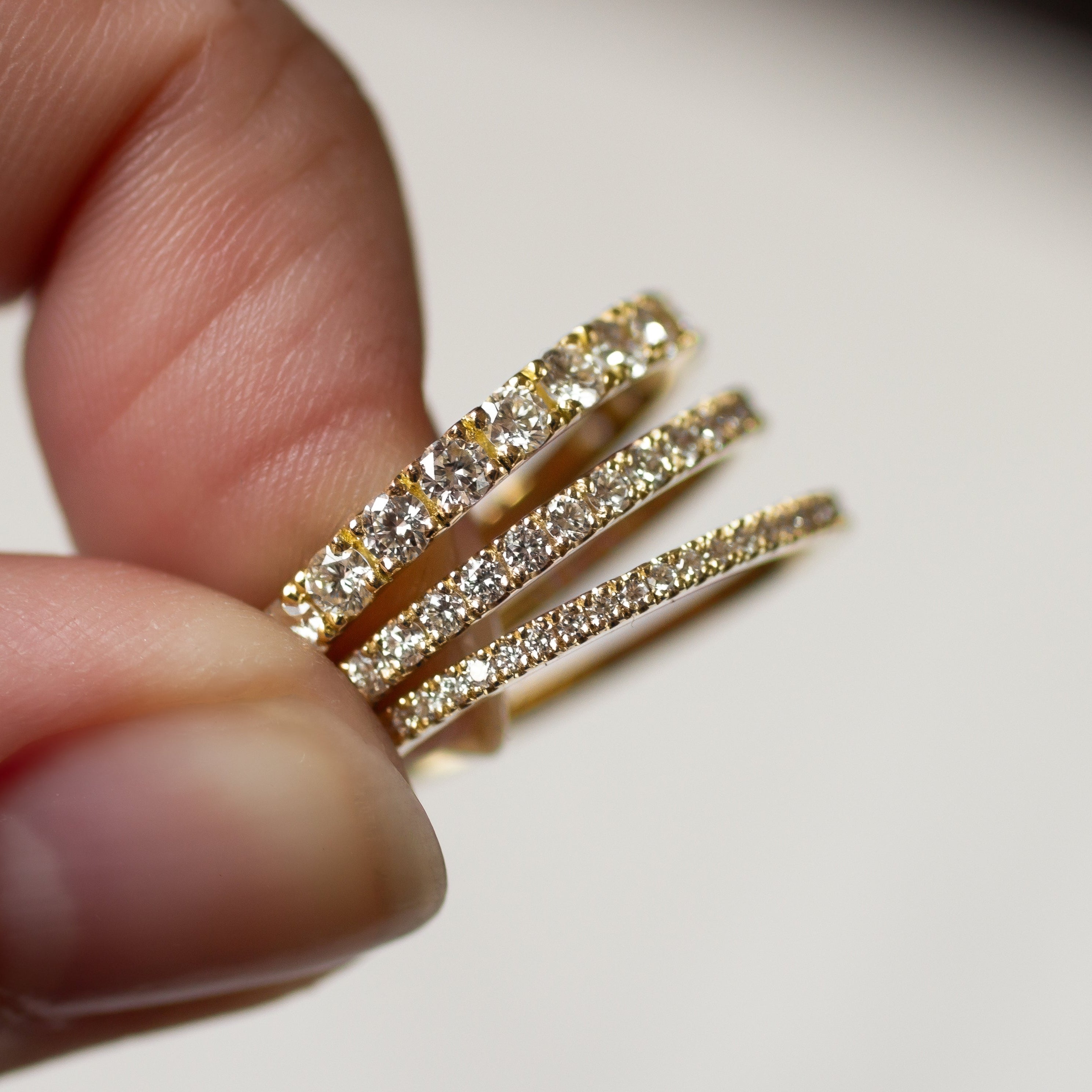 Half eternity wedding rings in three widths with diamonds held between fingers against a neutral background
