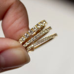 Half eternity wedding rings in three widths with diamonds held between fingers against a neutral background