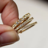 Half eternity wedding rings in three widths with diamonds held between fingers against a neutral background