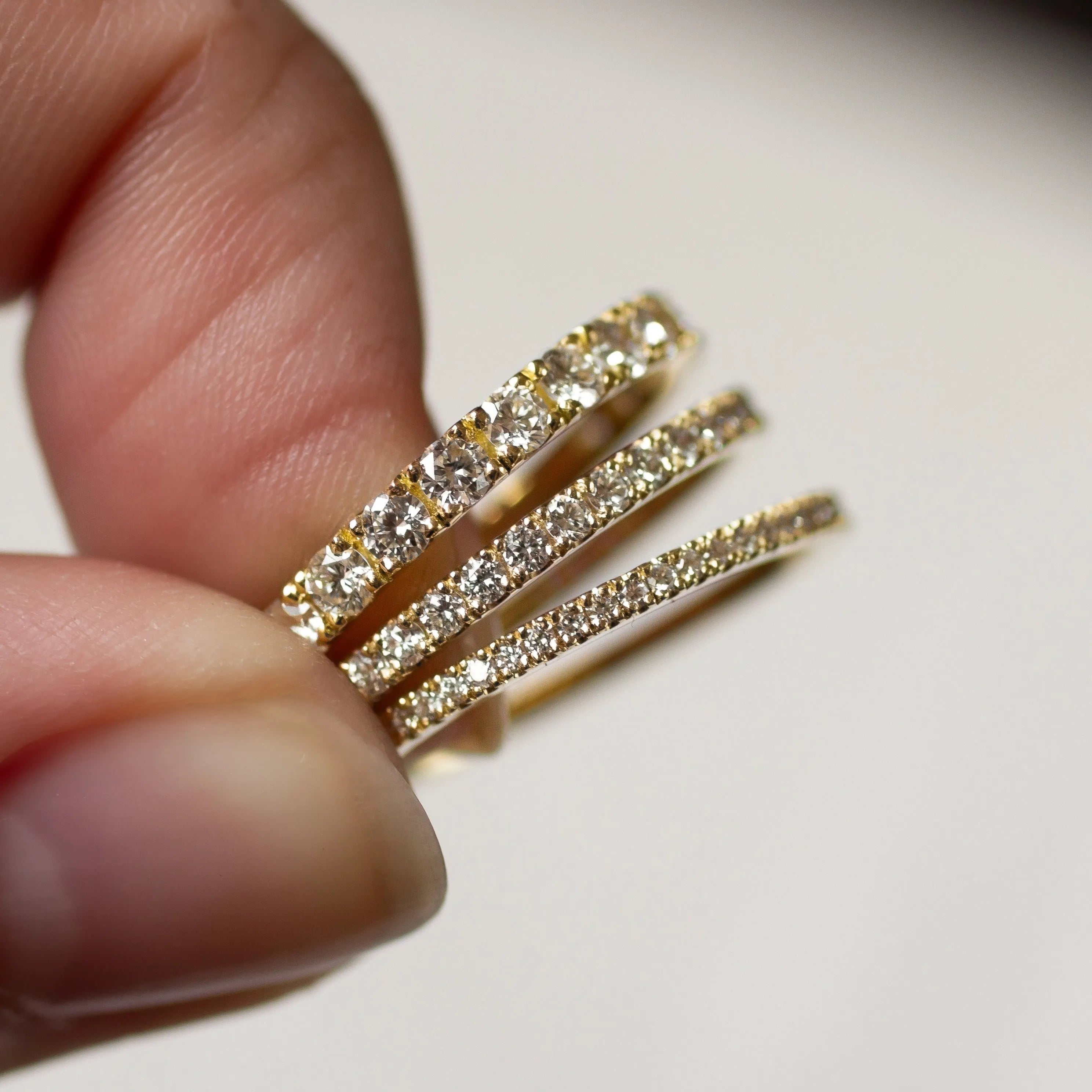 Half eternity wedding rings in three widths with diamonds held between fingers against a neutral background