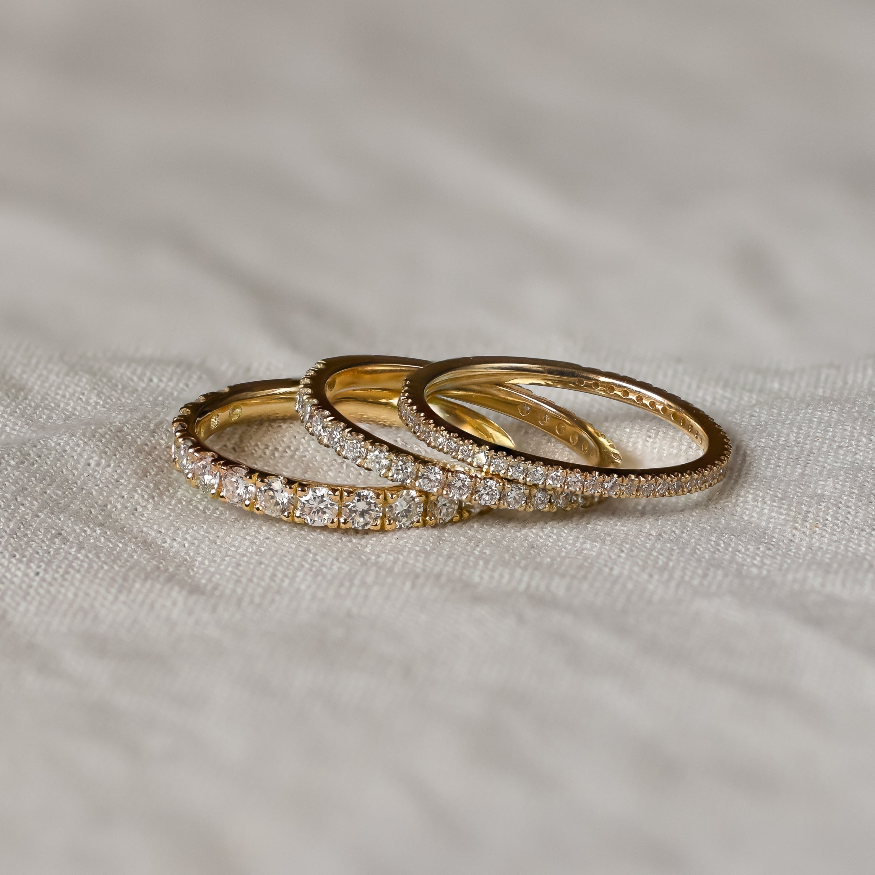 Three gold half eternity wedding rings with diamond accents on a textured fabric surface