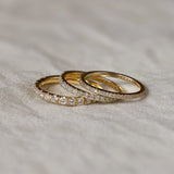 Three gold half eternity wedding rings with diamond accents on a textured fabric surface