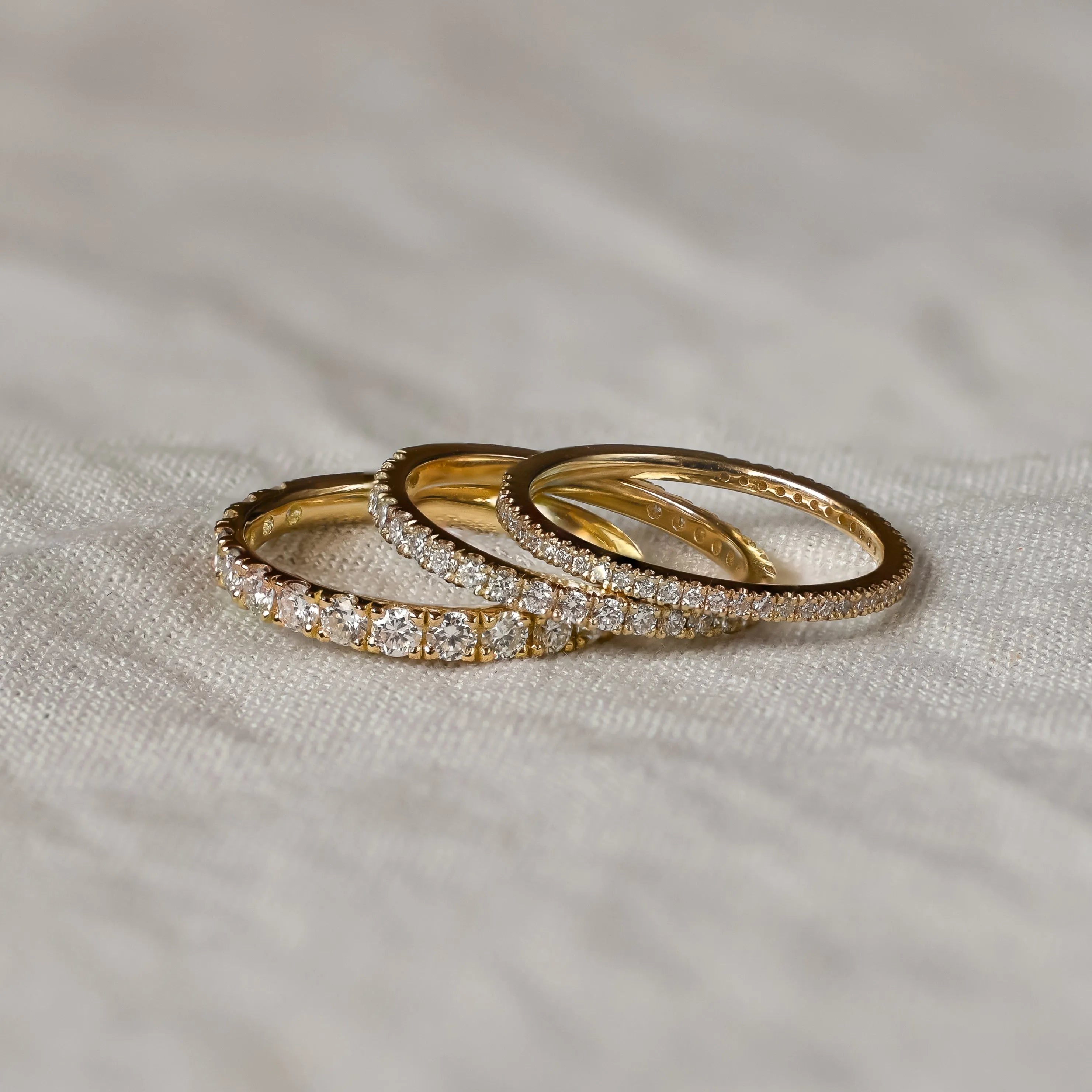 Three gold half eternity wedding rings with diamond accents on a textured fabric surface