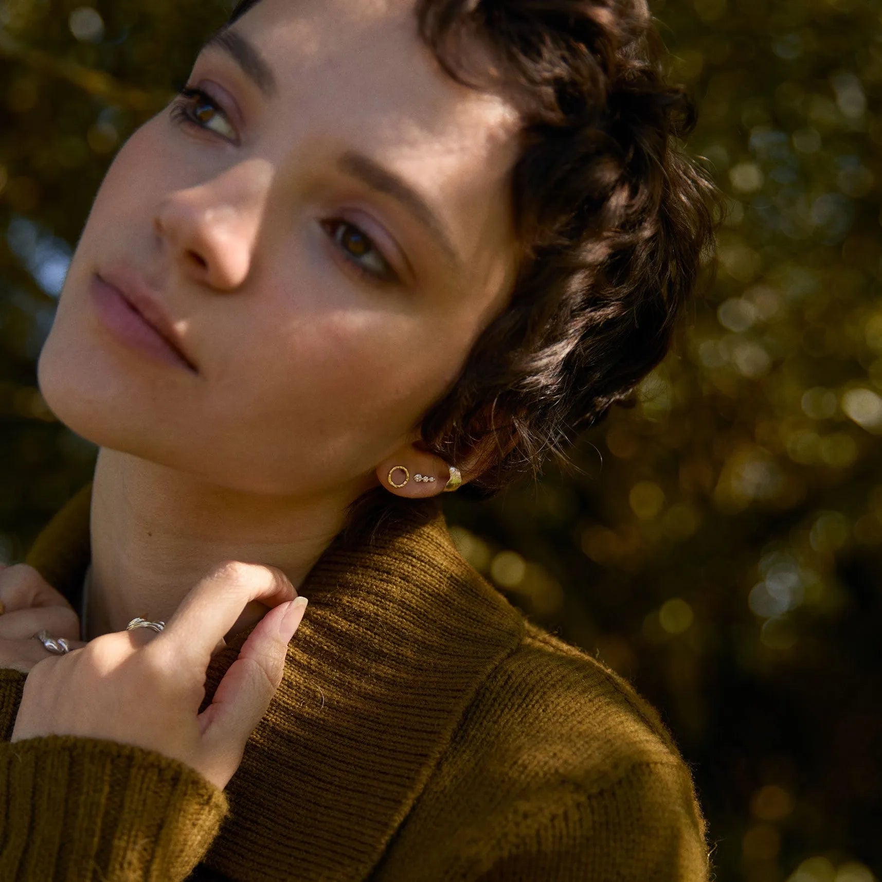 model outside wearing dark green jumper and circle earrings with diamond studs
