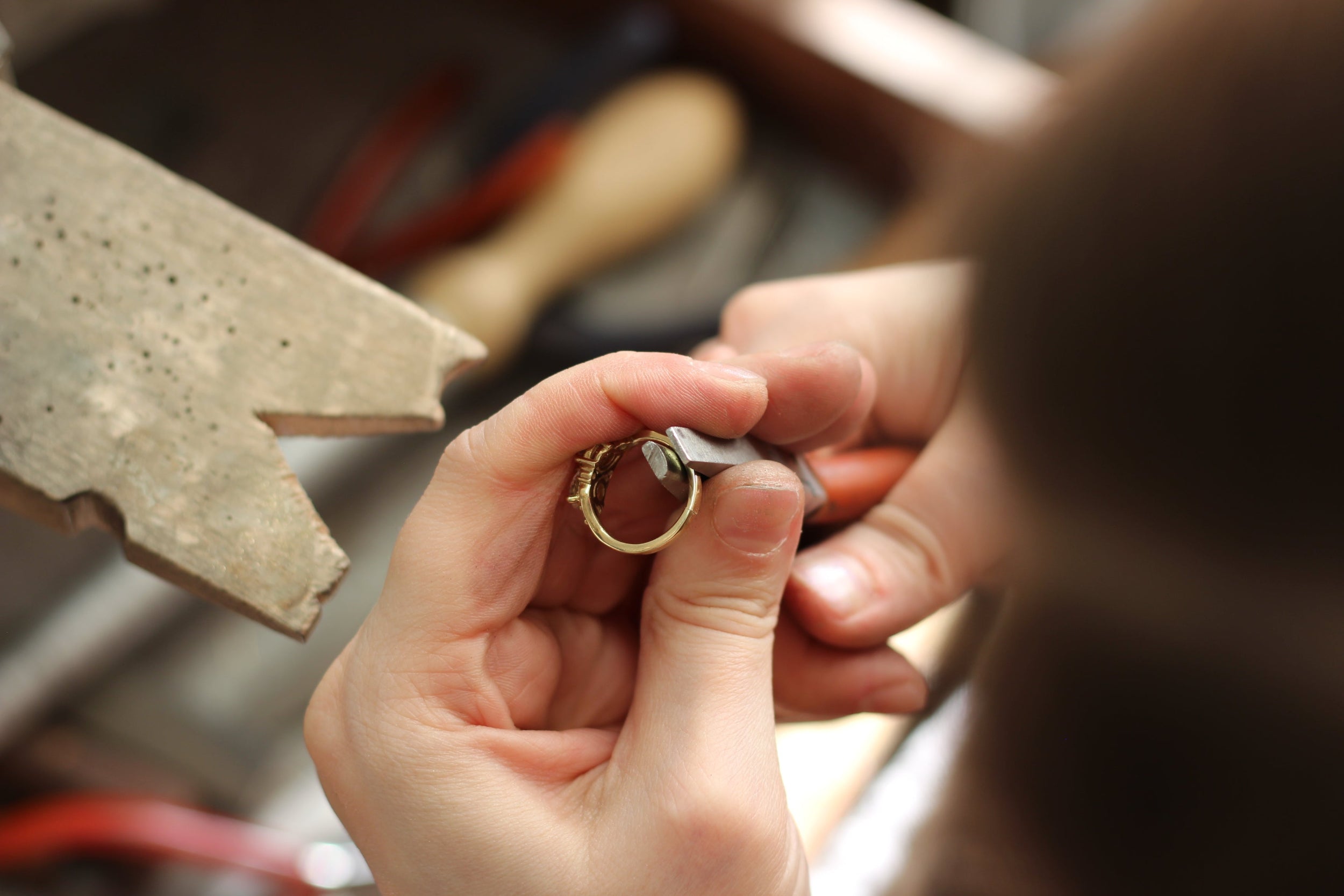 Close-up of hands holding a gold ring with tools in the background
