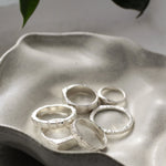 handmade silver rings in different textures on a wavy ceramic dish with leaves