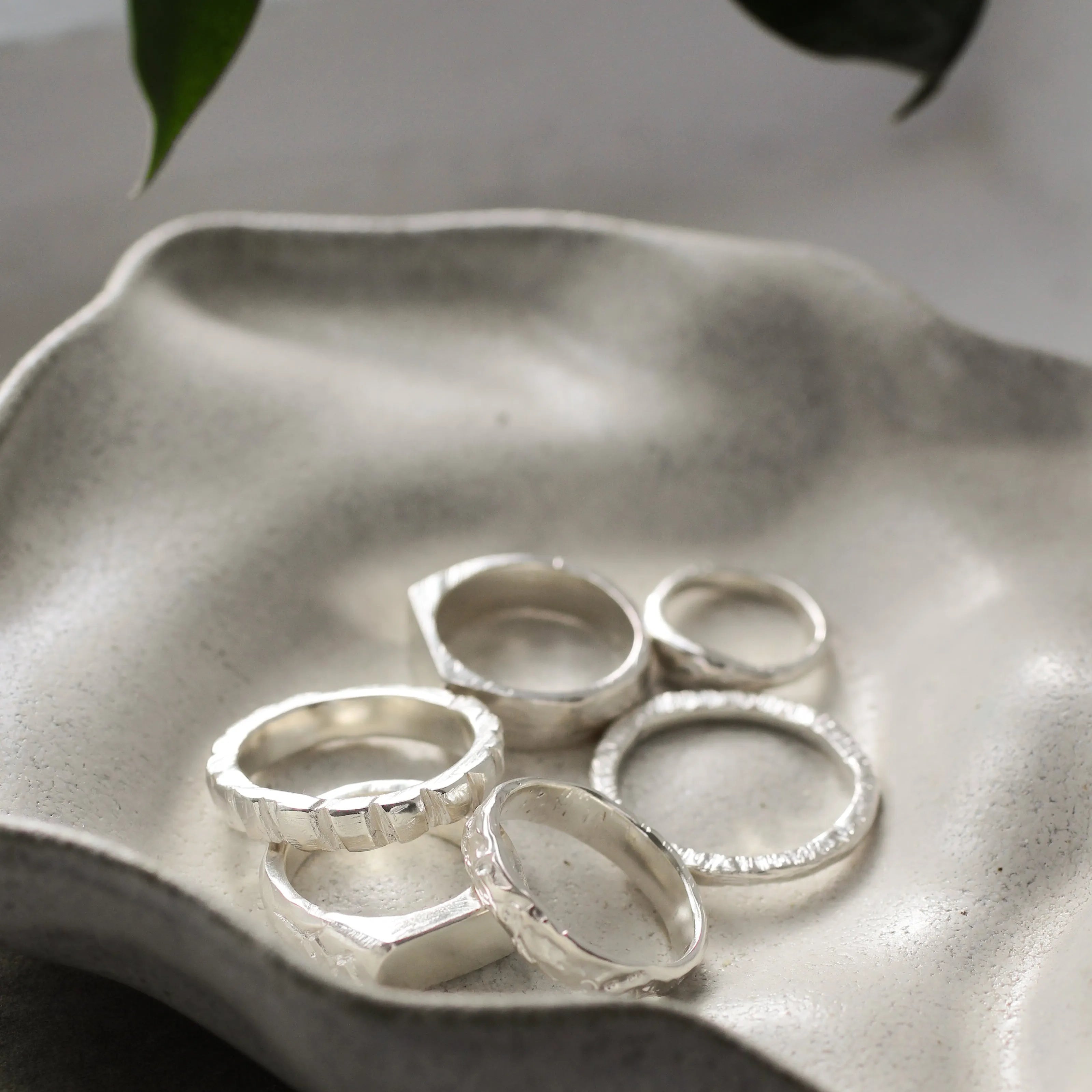 handmade silver rings in different textures on a wavy ceramic dish with leaves