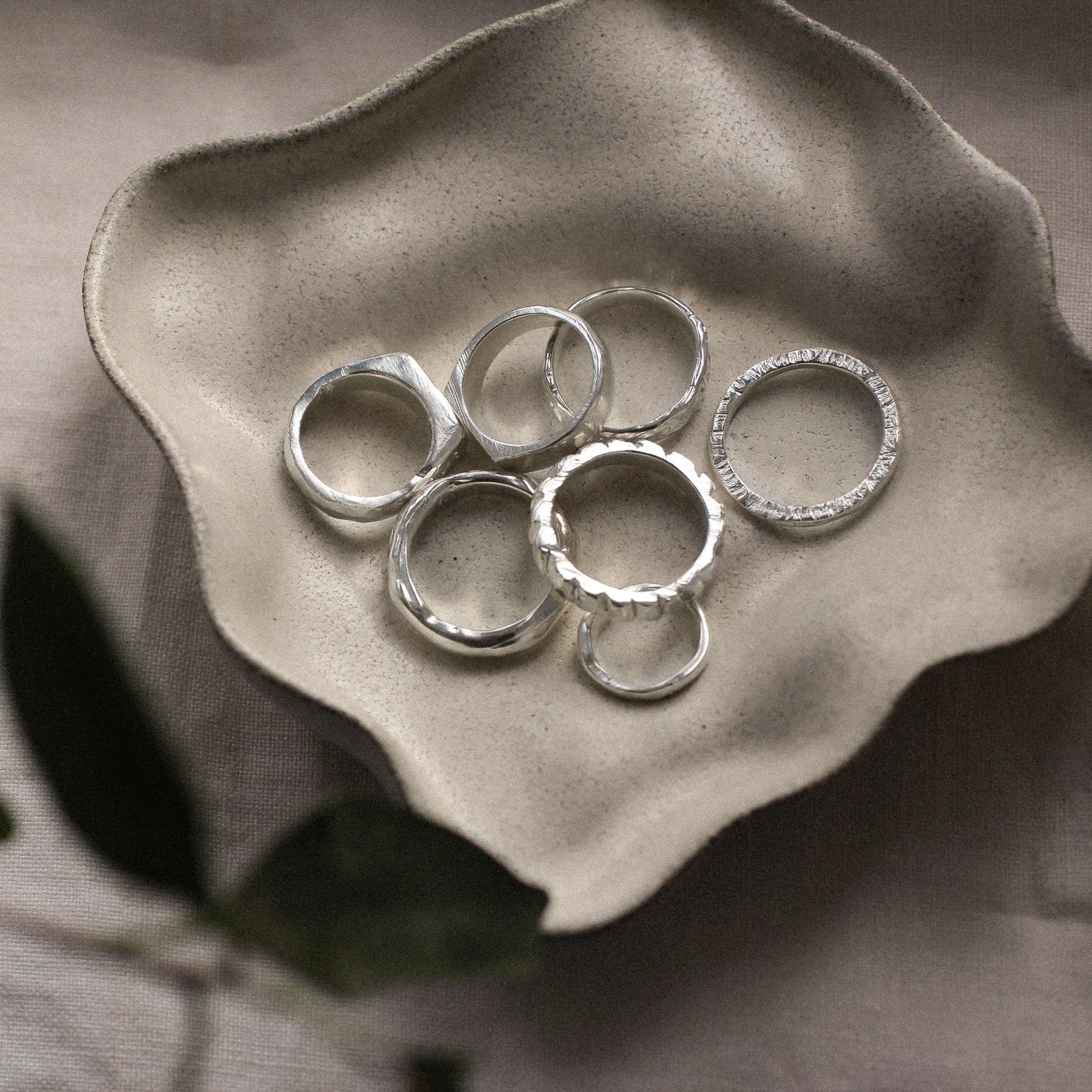 silver handmade rings on a dish with leaves in the foreground