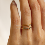 Gold v shaped wedding ring on a hand with size labels '1.3mm' and '2mm' on a beige background