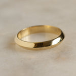 close up of knife edge wedding ring in gold on a marble surface