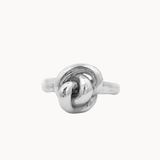 A polished silver ring featuring a sculpted knot design on a plain, light off-white background.