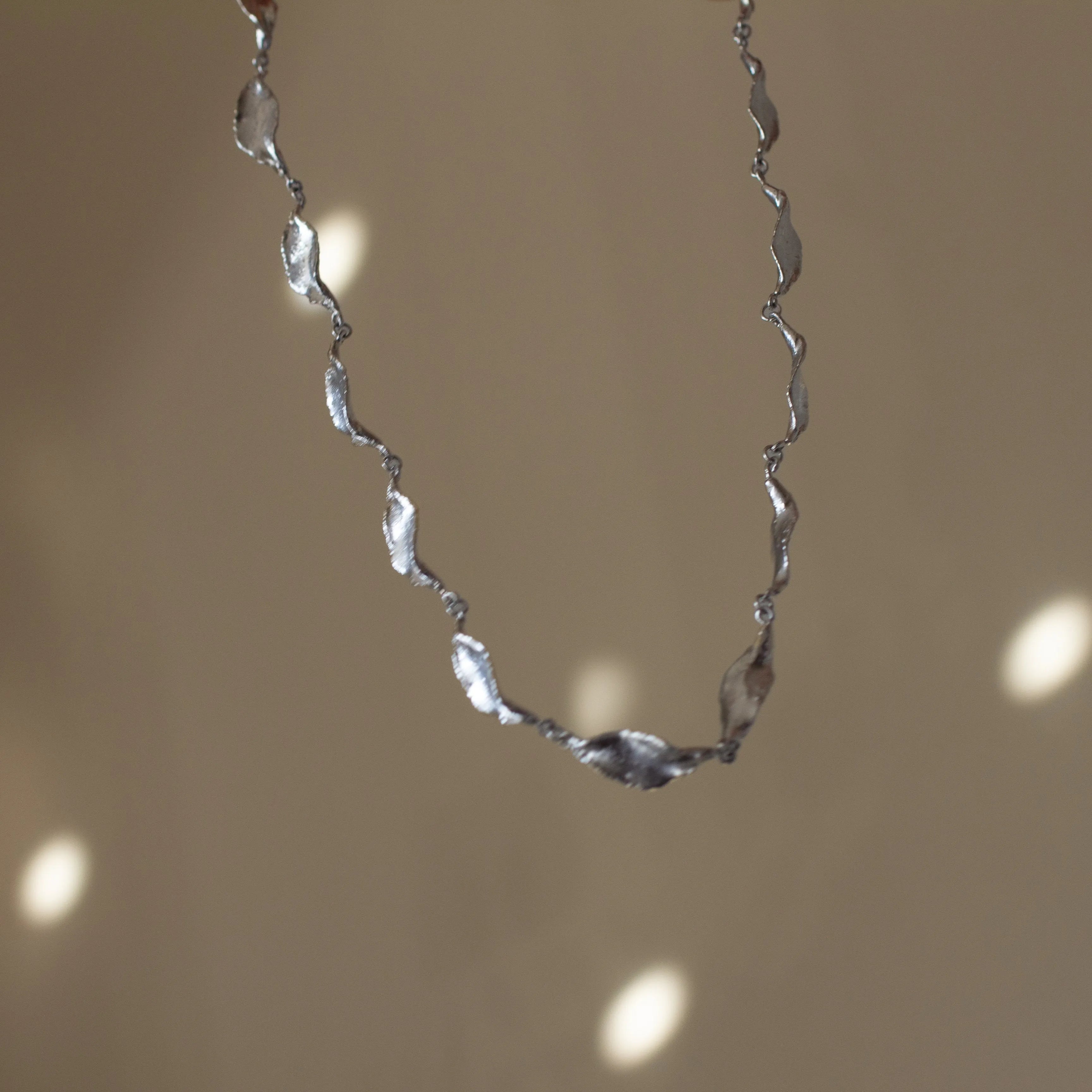 silver leaf chain necklace in motion with disco ball reflections in background