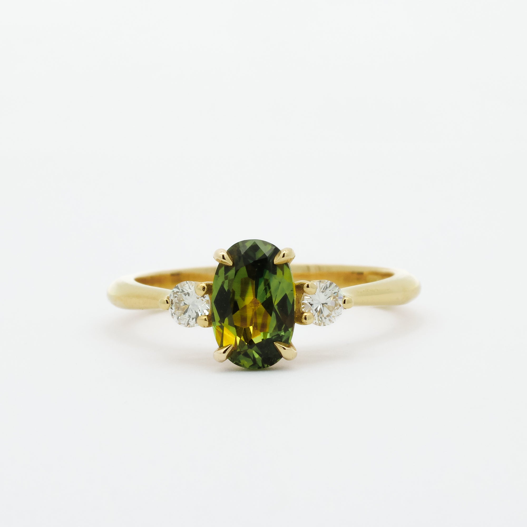 gold engagement ring with green yellow sapphire and round diamonds on a white background