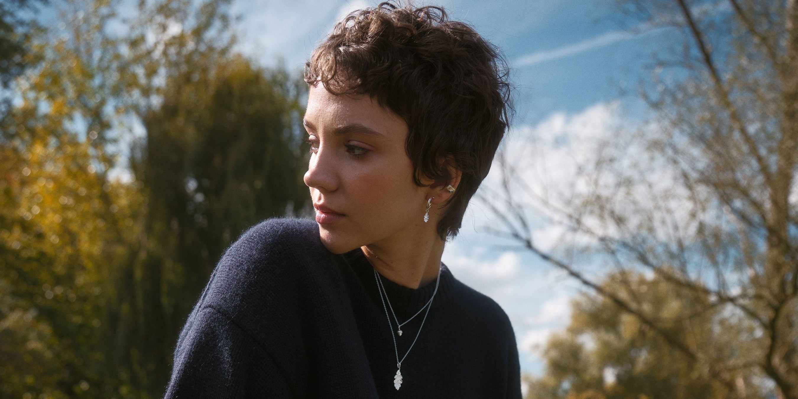 Woman sitting on a wooden fence in a natural setting with trees and grass.