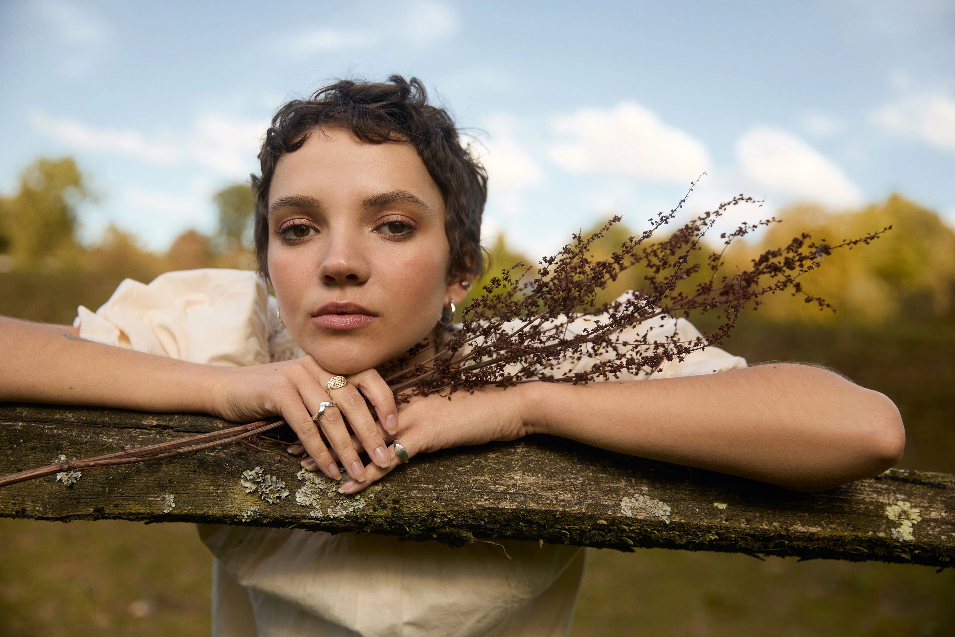 Woman with bouquet of flowers leaning on wooden fence outdoors wearing silver and gold rings