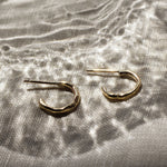 mini gold hoop earrings with molten organic texture on a fabric surface and light effects