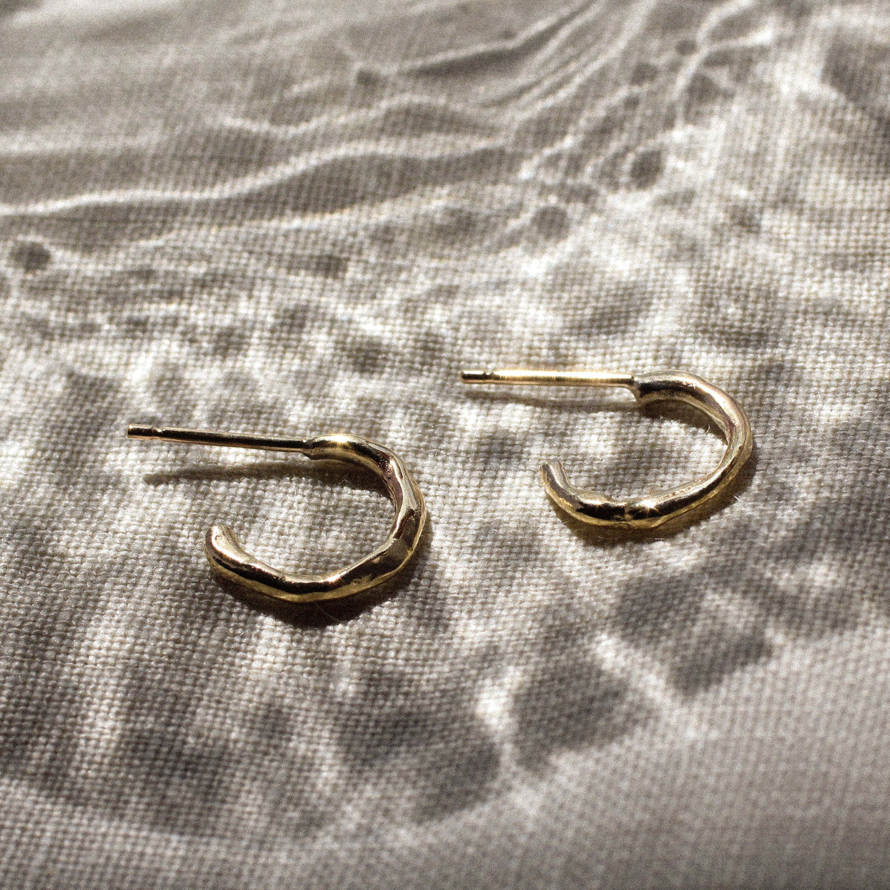 mini gold hoop earrings with molten organic texture on a fabric surface and light effects