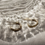 mini gold hoop earrings with molten organic texture on a fabric surface and light effects