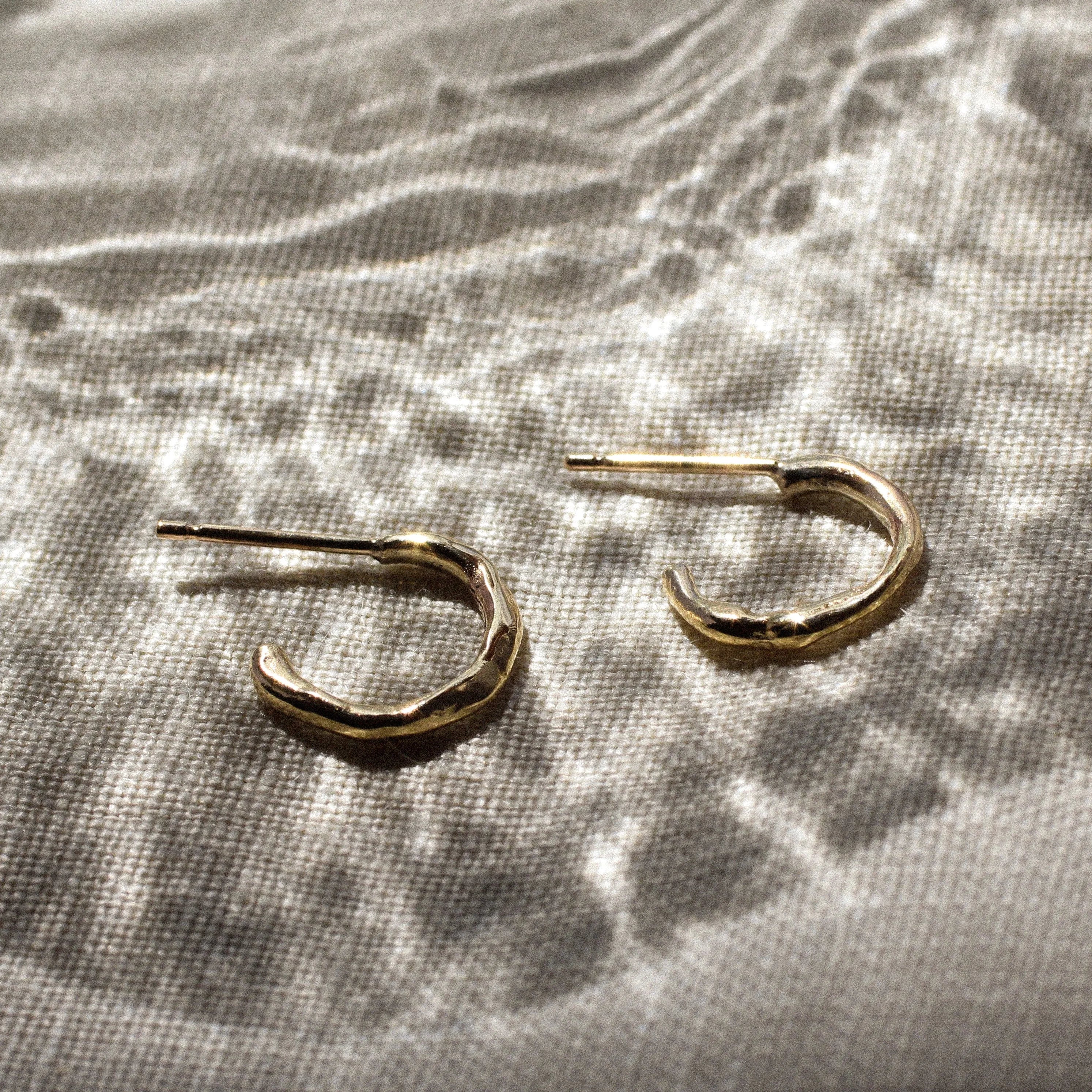 mini gold hoop earrings with molten organic texture on a fabric surface and light effects