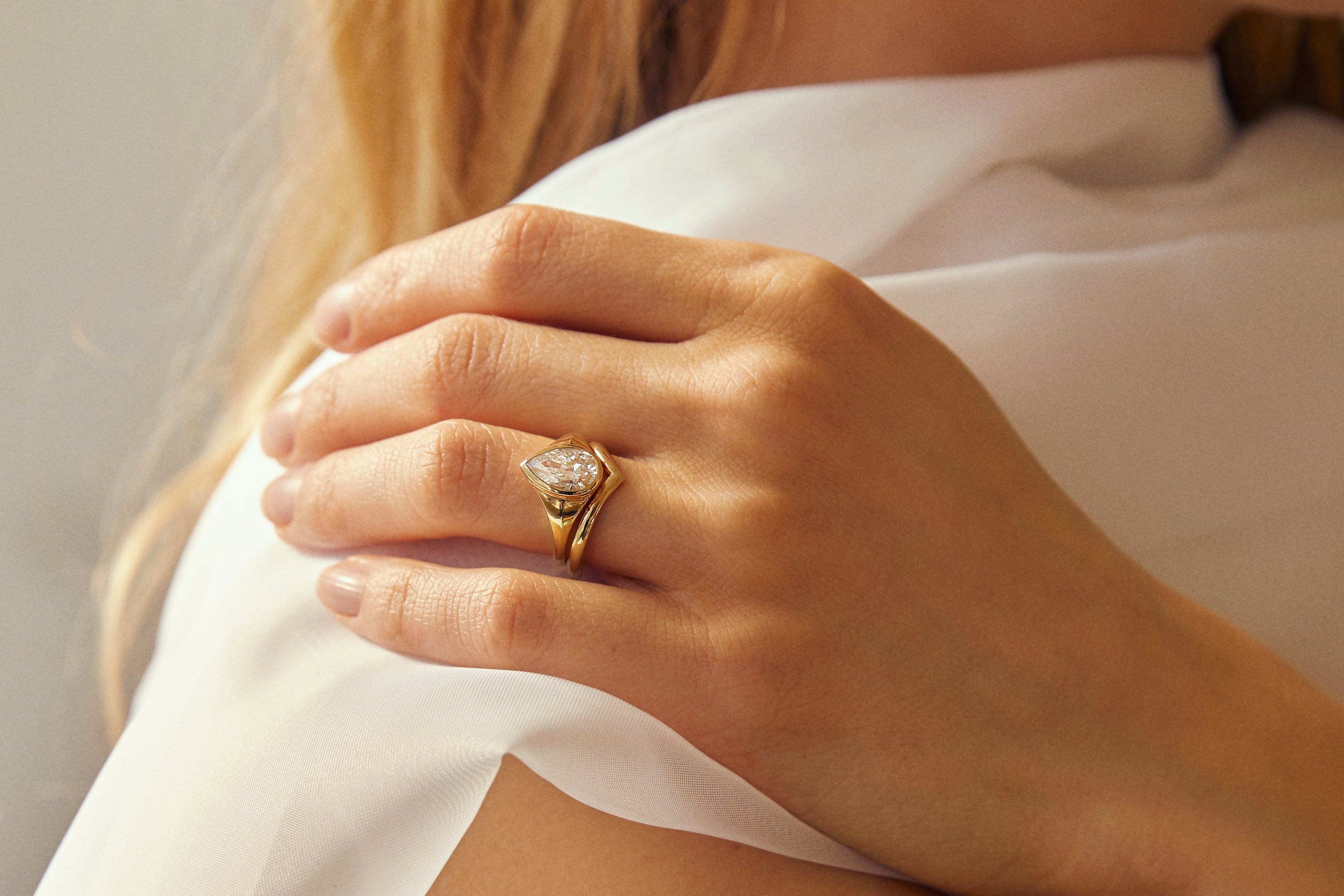 close up of hand wearing low set pear diamond engagement ring with curved nesting wedding ring