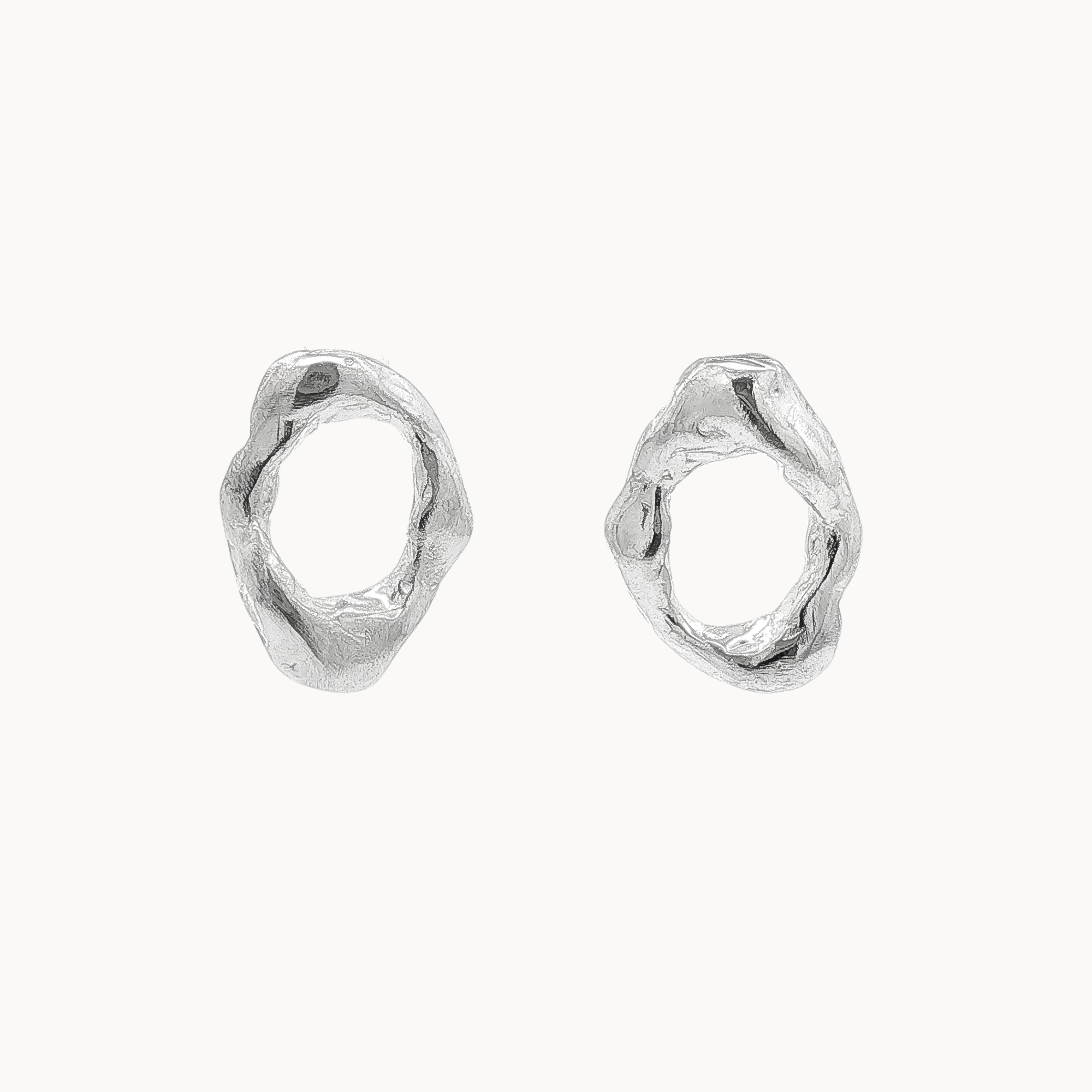 A pair of textured, organic open oval-shaped silver stud earrings on a clean, off-white background.