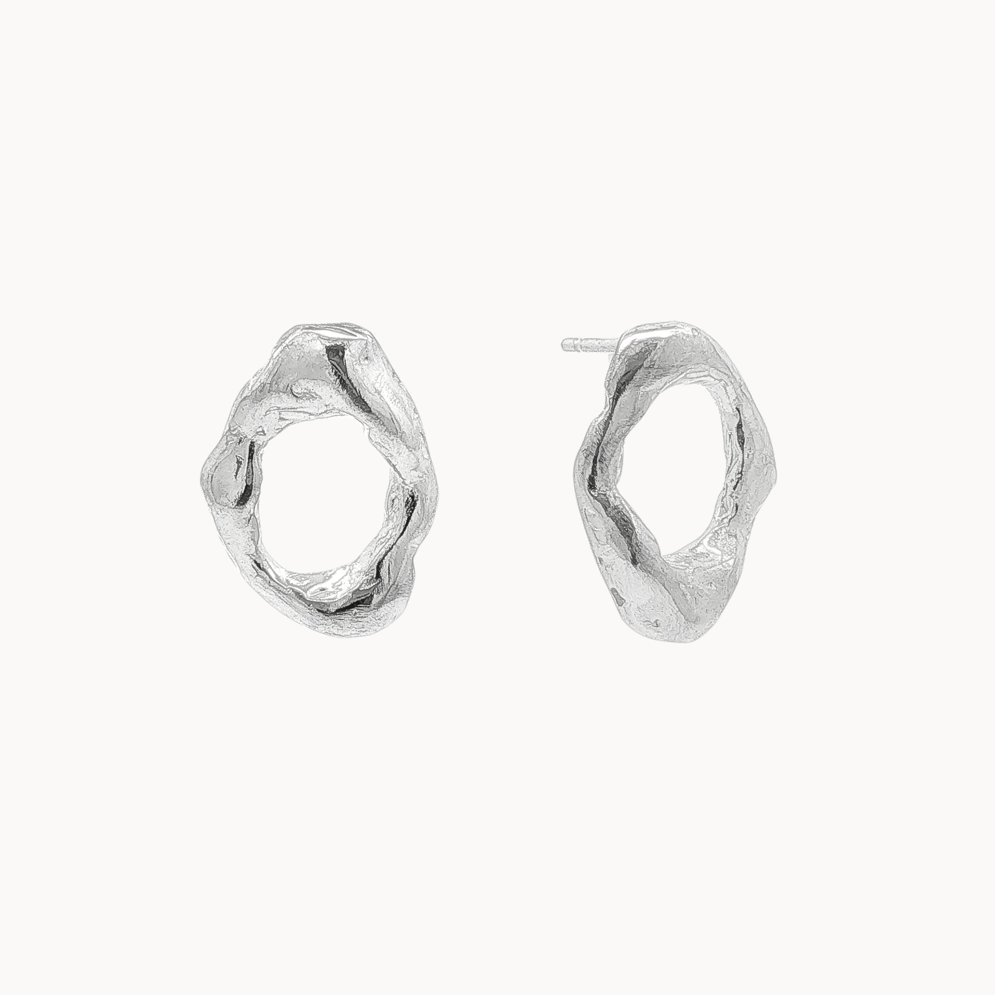 A pair of textured, organic oval silver stud earrings on a clean, off-white background.