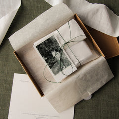 gift wrapped jewellery in a envelope with green twine, ribbon, blank notecard and print out picture of woman holding her child outside