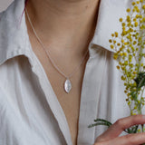 Person wearing a silver necklace with a leaf pendant, holding yellow flowers.