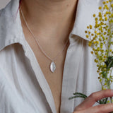 Person wearing a silver necklace with a leaf pendant, holding yellow flowers.