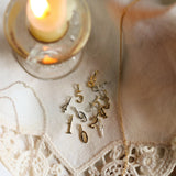 Gold necklace with various number pendants on a lace fabric with a lit candle in the background