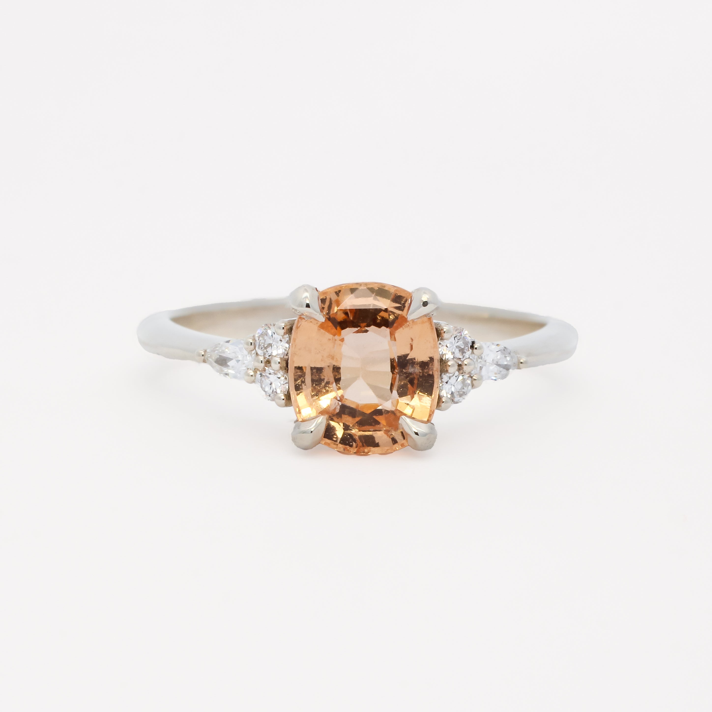 white gold engagement ring with a large orange gemstone and smaller diamonds on a white background