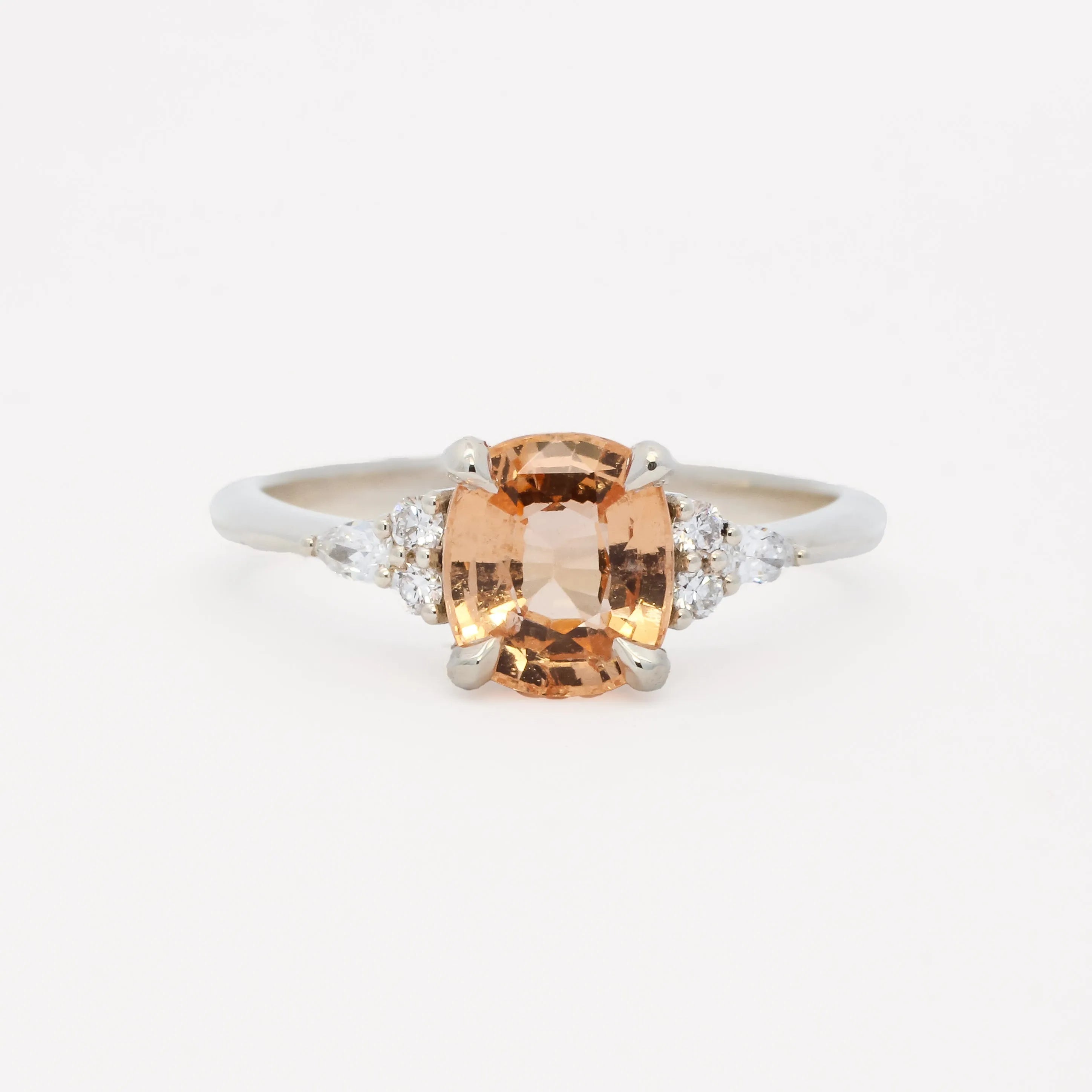white gold engagement ring with a large orange gemstone and smaller diamonds on a white background
