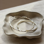 Silver bangles on a textured ceramic dish with a neutral background