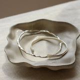 Silver bangles on a textured ceramic dish with a neutral background