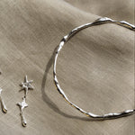 close up of silver organic bangle and a silver star dangle earring on a beige fabric