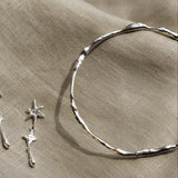close up of silver organic bangle and a silver star dangle earring on a beige fabric