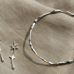 close up of silver organic bangle and a silver star dangle earring on a beige fabric