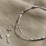 close up of silver organic bangle and a silver star dangle earring on a beige fabric