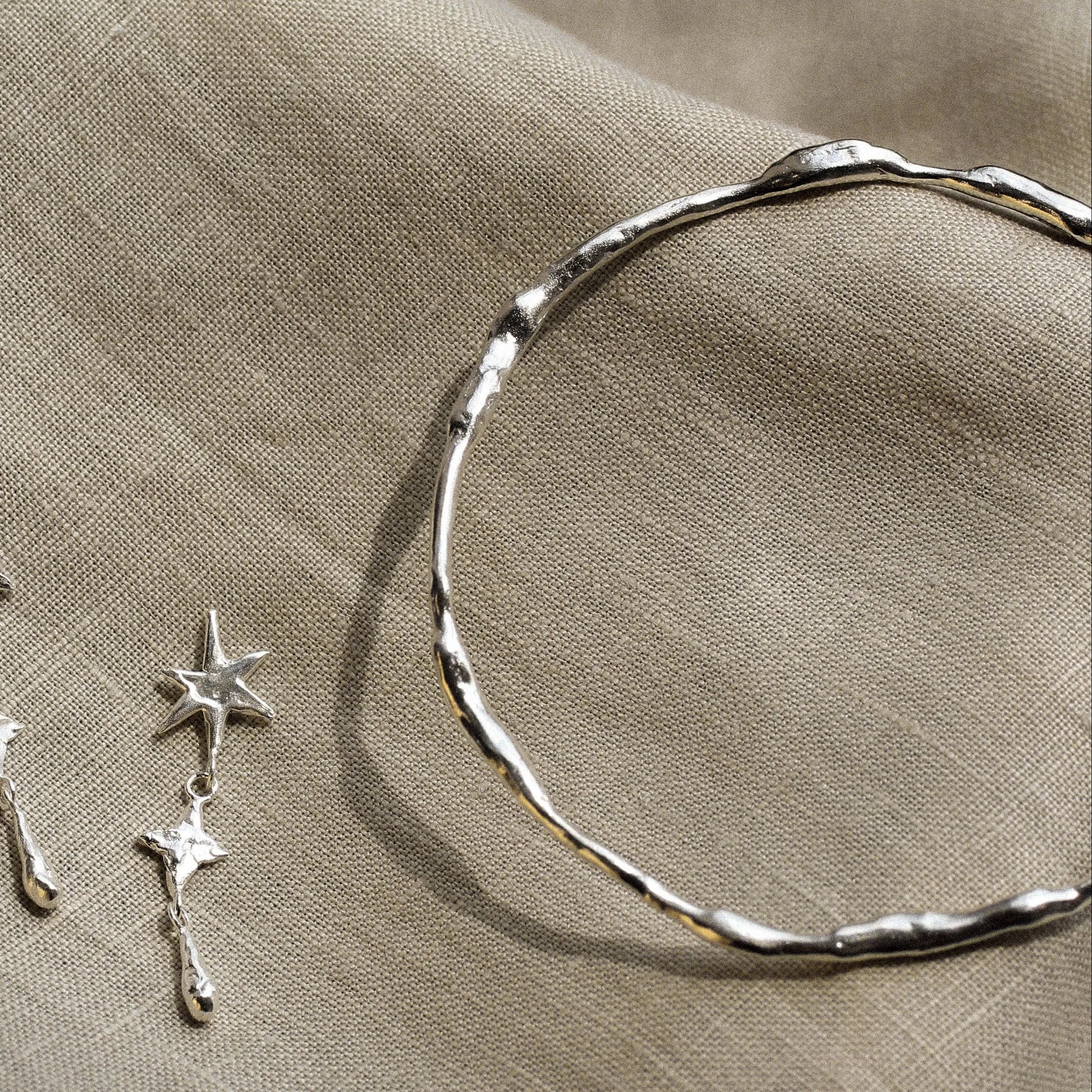 close up of silver organic bangle and a silver star dangle earring on a beige fabric