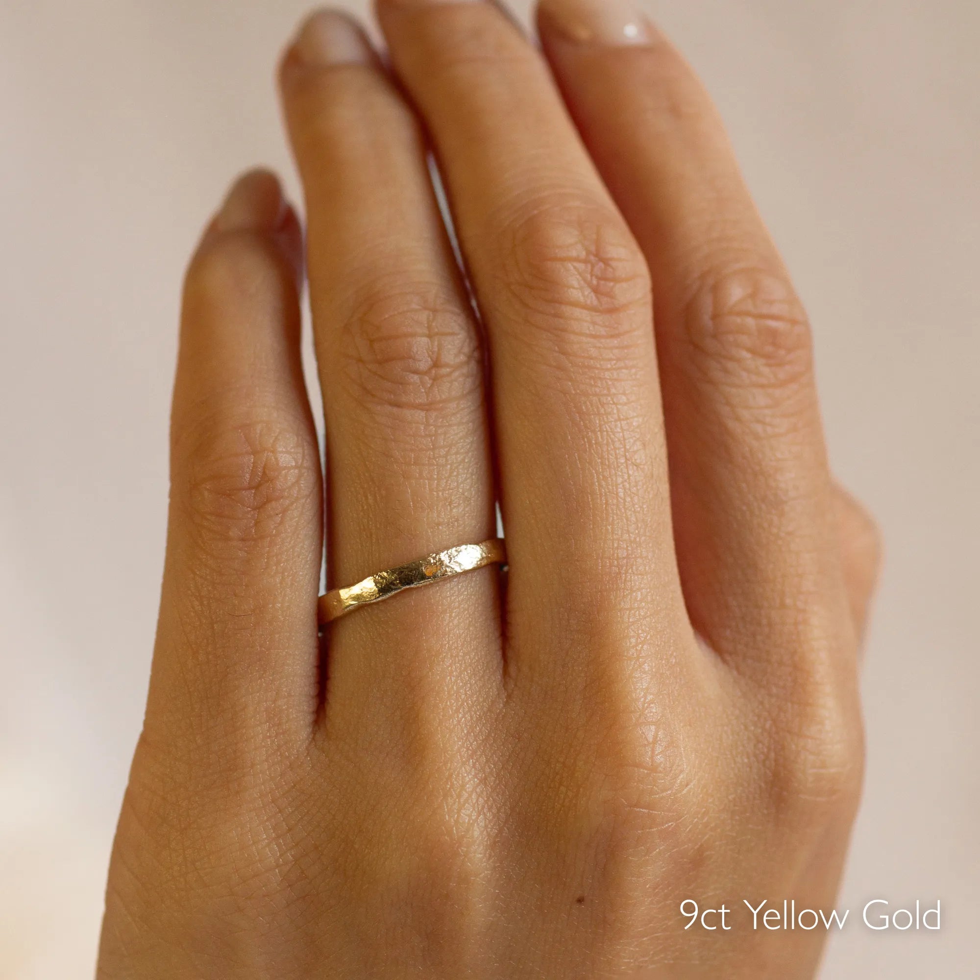 Gold organic rustic wedding ring with 2mm width on a hand with '9ct Yellow Gold' text