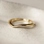 Gold ring with wavy design and textured, worn finish on a light stone surface