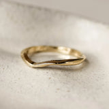 Gold ring with wavy design and textured, worn finish on a light stone surface