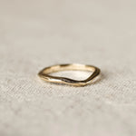 Gold ring with soft curve design and organic finishon a textured beige fabric background